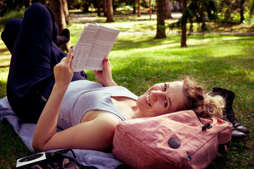 Caroline reading a book in a park and smiling into the camera